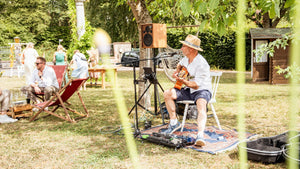Live-Musik unter schattigen Bäumen: Ein Gitarrist sorgt im Garten des Weingut Robert König für eine entspannte, sommerliche Atmosphäre, während die Gäste im Hintergrund das Fest genießen.