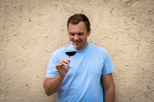 Weinliebhaber Philipp König genießt das Aroma eines Spätburgunder-Rotweins und riecht konzentriert an seinem Weinglas, stehend vor einer hellen Strukturwand.