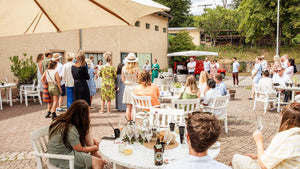 Gemeinsamer Moment im Innenhof des Weingut Robert König: Unter einem großen Sonnensegel versammeln sich die Gäste, während an den weißen Tischen Wein, Gläser und sommerliche Leckereien bereitstehen.